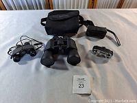 Three pairs of binoculars displayed on a table with two black carrying cases behind them.