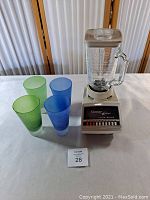 Vintage Osterizer Galaxie blender with clear glass jar and six frosted glasses in blue and green colors on white surface.