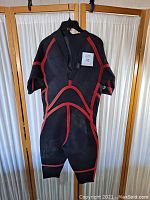 Full view of vintage O'Neill wetsuit hung on a hanger showing black neoprene material with red seam trim and signs of wear.