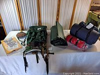 Wide view of camping equipment on table showing backpack, sleeping bag, blanket, canteen, and pad