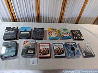 Photo showing all DVD box sets arranged in two rows on a table. Titles visible include Six Feet Under, Spin City, Family Guy, The Addams Family, Quantum Leap, and others.