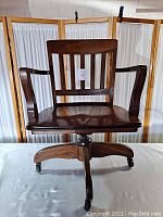 Front view of the vintage wooden desk chair showing armrests, slatted back, and 4-point base with casters.