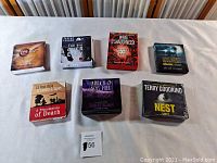 Photo of seven suspense audiobook CD box sets arranged on white surface showing front cover art and title.