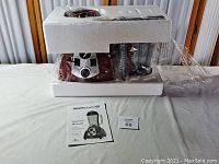 Photo showing the blender packed in white foam packaging with blending jar and other accessories visible, placed on a white surface with accompanying owner's manual visible.