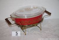 Red Pyrex glass bowl with white and gold floral design inside steel buffet server frame with brass finish and wooden handle ends