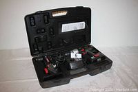 Open plastic carrying case containing two Craftsman cordless drill-drivers, charger, battery, and instruction manual on a fabric surface.