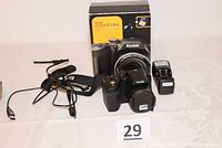 Front view of Kodak EasyShare Z5010 camera with lens, charger, strap, USB cable, battery, and original box on display.