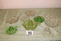 All nine glass juicers displayed together showing two green, one Vaseline and six clear juicers, arranged on a green cloth.