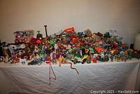 Wide view of assorted small toys spread across a table including animals, action figures, and many colorful toys.