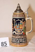 Left side view of the handmade and hand painted Prague beer stein with lid, showing detailed imagery and inscription.