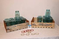 Overall lot with Ball Mason Jars in blue glass inside two vintage "Table Grapes of California" carriers, along with rubber rings and glass lids displayed in front.