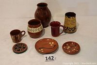 Photo of all 8 items: two vases, tall mug, two plates, two cups, and trivet arranged together on white surface.