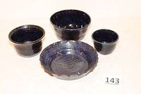 Four cobalt blue pottery bowls arranged together showing size variation, glossy finish, and scalloped edge on largest bowl.