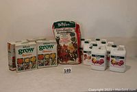 Overview photo of lot showing 4 boxes of Burpee Grow Flower Fertilizer, 6 plastic bottles of Burpee Flower or Rose Fertilizer, and 1 large bag of Burpee Azalea, Camellia, Rhododendron feed fertilizer