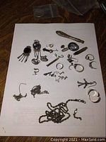 All items spread on white paper showing earrings, rings, handle piece, and chains in varying condition.
