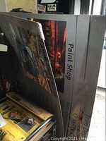 Close view of one plastic backed sign showing text and photo for Paint Shop section, mounted on a frame with visible wear and dust.