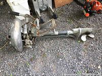 Full side view of vintage Champion boat motor showing propeller, mounting bracket, and motor body on gravel surface.