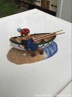 Side view of the Department 56 figurine showing both men hauling the wooden rowboat out of water onto sandy shore.