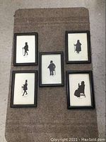Top view of 5 framed black silhouette prints arranged together on carpeted floor. Each frame is rectangular with glass front and dark border.