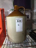 Front-side view of 1 gallon stoneware jug with sticker label showing lot number. Jug has glossy brown top and handle, lighter beige lower body.