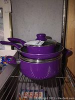 Photo showing stacked purple pots and frying pan with lids on metal rack.