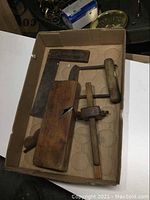 Box containing wooden hand plane, chop/sinker tool, wooden Stanley scribe, and wooden & brass square