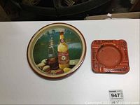 Photo showing the round metal bar tray with beer bottle and glass design on the left and the orange square Reinhardts ashtray on the right.