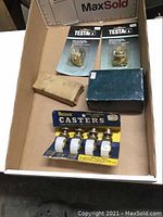 Top view of all items in a box: two drawer lock packages, one small brass hinge box, one blue box likely for the double action hinges, and a pack of four Bassick casters with white wheels on card backing.
