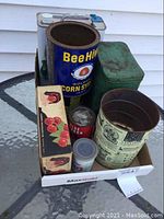 Photo showing the full collection of vintage metal tins and cardboard box arranged on a glass table outside, highlighting their sizes and shapes.