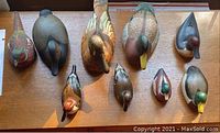 Overview of seven wooden duck decoys, one wooden pheasant decoy, and one porcelain duck figurine arranged on table