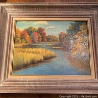 Frontal view of the framed autumn landscape painting showing river and trees.