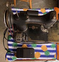 Top view of the vintage black Singer sewing machine with the motor and foot pedal on a pineapple patterned cloth.