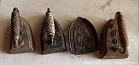 Four items displayed: three flat cast iron clothes irons with different handle styles and marks, one decorative cast iron trivet.