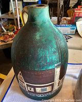 Photo of large folk art hand painted jug showing countryside scene with trees and cottages, blue-green background