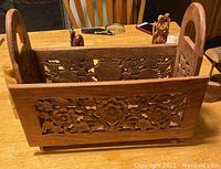 Front view of the wooden magazine holder with intricate floral and bird cutouts and rounded handles