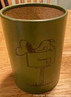 Front view of olive green pencil cup holder with Snoopy lying on a mailbox graphic