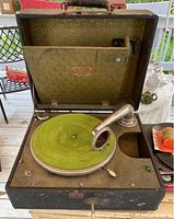 Open vintage Cub Carryola record player showing green felt turntable and metal tonearm.