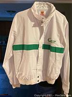 White new old stock Quaker State racing jacket with green stripe and embroidered logo, hanging on a hanger under indoor lighting.