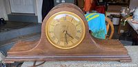 Front view of wooden antique mantle clock with gold-colored dial and broken glass