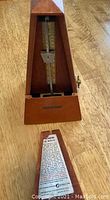 Front view of the metronome showing the pendulum, scale, and pyramid walnut wood case.