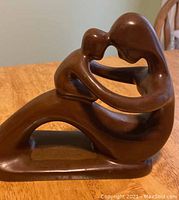 Side view of the wood carving showing the curved lines and intertwined figures of the mother and child.