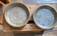 Two metal pie tins embossed with 'New England Flaky Crust Pie Table Talk' placed on top of wooden crate