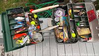 Full open green tackle box showing over 50 assorted vintage fishing lures and accessories including bobbers, fishing line, and various lure types