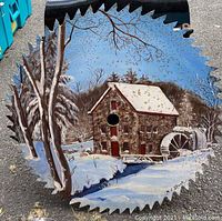 Full view of the sawmill blade showing the painted winter scene of the stone mill with water wheel and surrounding snow-covered landscape.