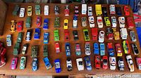 Overview of 70+ small diecast cars including various colors and models placed on wooden surface, showing range of toy vehicles