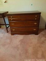 Front view of wooden four drawer chest with two smaller top drawers and two larger bottom drawers with brass handles on carpeted floor