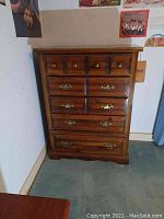 Front view of the wooden dresser showing five drawers with metal knobs and brass handles.