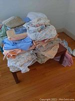 Two photos showing stacks of mixed bedsheets on a small wooden table in a room with hardwood flooring.