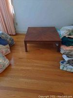 Photo showing the full square coffee table on wooden flooring with surrounding household items.
