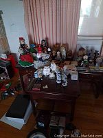 Photo showing assortment of dolls, figurines including international dolls, oriental figures, cats and dogs, paperweight, plaques, music box, and postcards on tables.